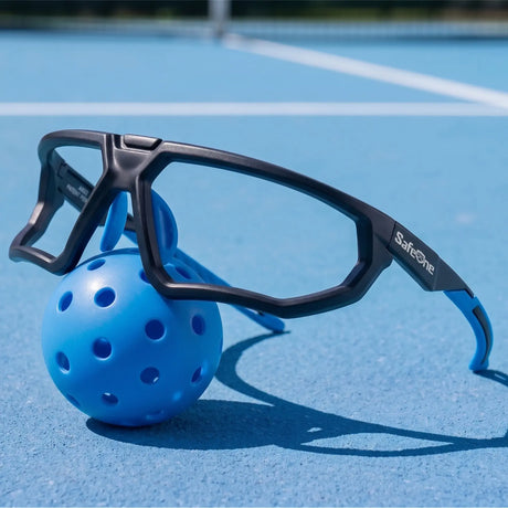 SafeOne AEGIS Phantom Black glasses resting on a blue pickleball on an outdoor court