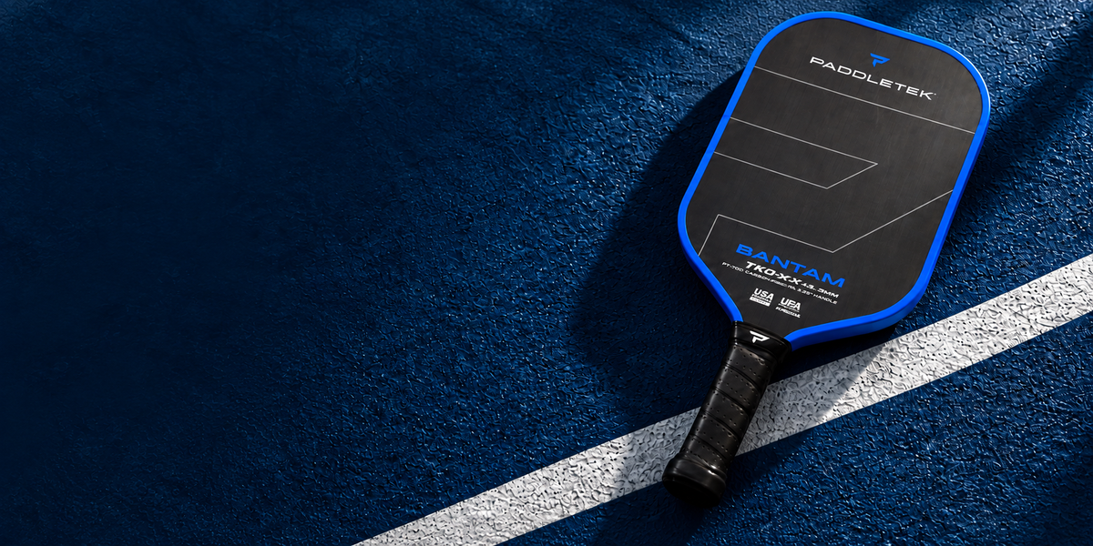 Blue Paddletek paddle on a navy pickleball court